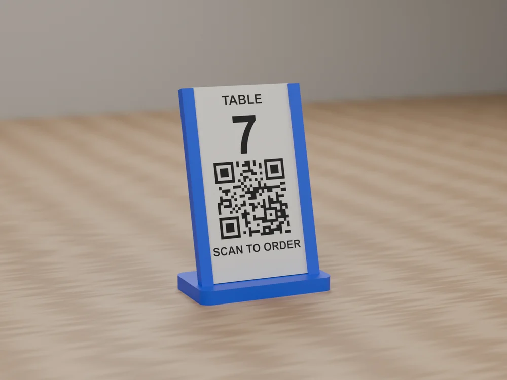 A blue 3D printed QR code stand on a wooden table, holding a white card that reads TABLE 7, a QR code and SCAN TO ORDER